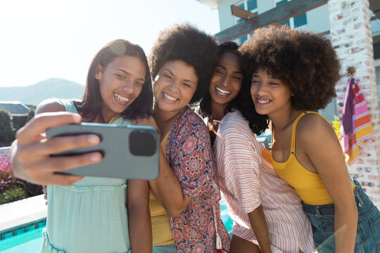Carefree biracial female friends taking selfie over cellphone while having fun at poolside in summer