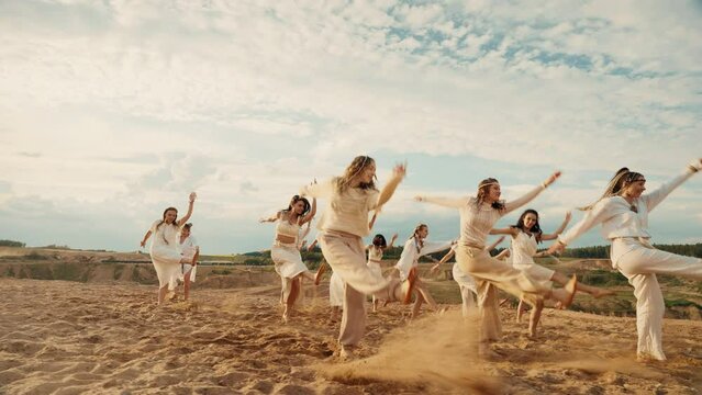 4k slow-mo group of women in white ethnic clothes dancing choreography on sand. Nature beautiful landscape. Blu sky and sunset light. Rural and boho style.