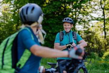 Naklejka premium Portrait of active senior couple riding bicycles at summer park, standing on path and looking at camera