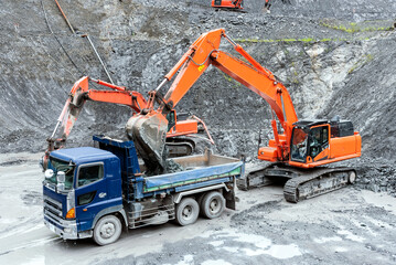Open pit quarry, excavator loading gravel on dump trucks: construction industry