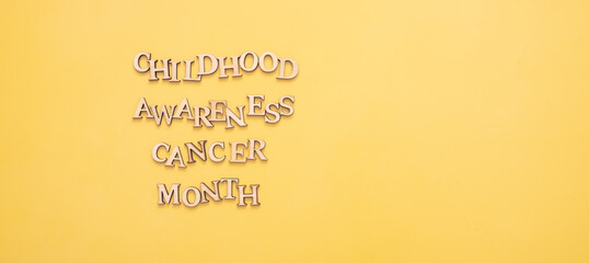 Childhood cancer awareness month text from wooden letters on yellow background with copy space
