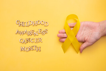 Childhood cancer awareness month text from wooden letters and female hand with yellow ribbon on...