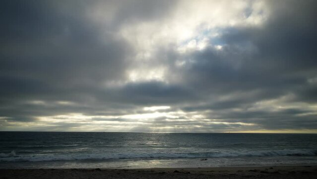 Ocean waves lapping as people in silhouette walk along Torrance Beach, California on a moody day - static wide angle time lapse