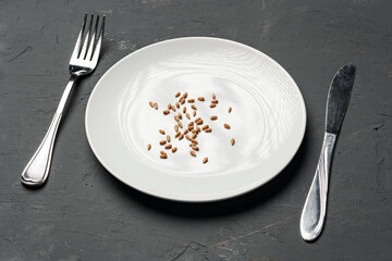 Concept of a global food crisis caused by hunger due to lack of grain. Plate with small amount of grain on plate on black background
