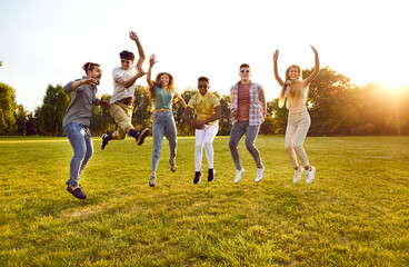 Group of several happy excited cheerful young diverse friends meeting up on warm sunny day in summer, spending time outside, having fun, and jumping on green field, meadow or park lawn all together