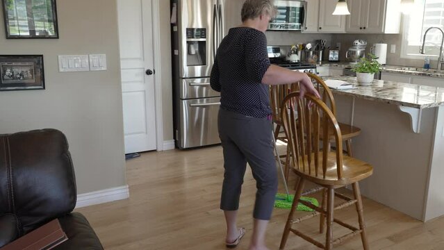 Senior woman cleaning her hardwood kitchen floors - tilt down