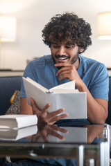 Curly-haired indian guy reading a book and looking involved