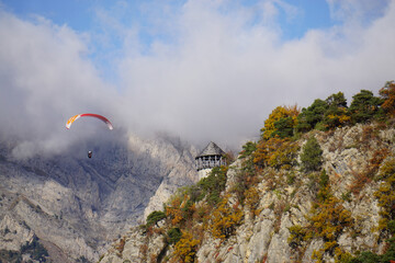 paraglider over the mountains and stone tower  in the fall in the alps france with fog lifting