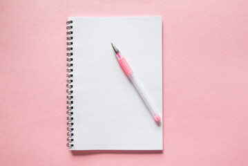 white notebook with a pen on a pink background. copy space.