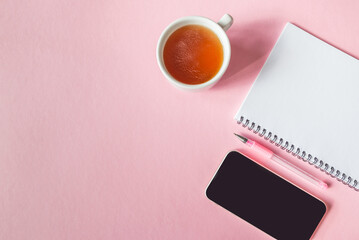 Top view photo of notepad, pen, tea cup and smartphone on pink background