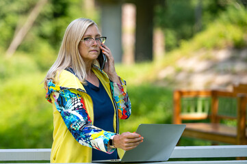 middle age woman at the garden working from home using laptop and speaking on the phone