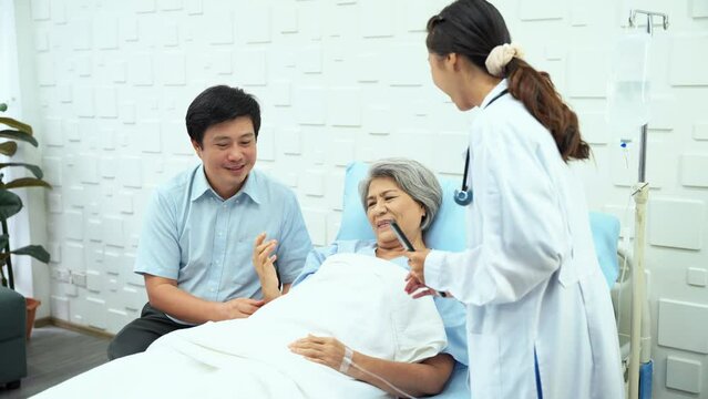Specialist female doctor come in for a physical examination and symptoms of elderly female patients lying in bed in the patient room. Elderly female patient show arms up showed improved symptoms.