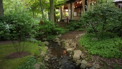 Beautiful lush green landscaping and flowing stream leading to an upscale luxury restaurant with flowing curtains.  Feelings of peace and luxury in the landscaping and architectural video.