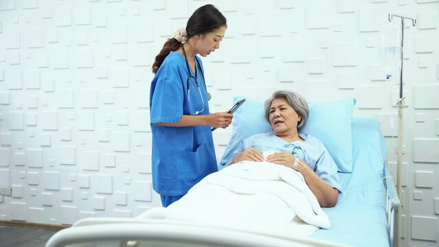 Female doctor enters patient room to inquire about the symptoms of an elderly woman who was receiving saline in a bed in the patient room. Female doctor talking to female patient about better.