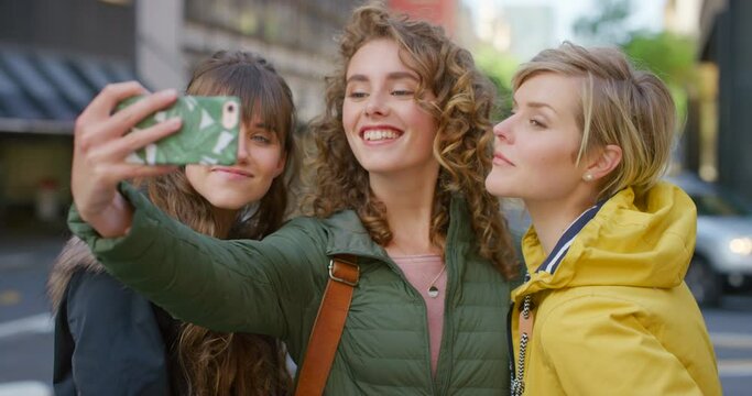 A group of friends on holiday making a selfie with a phone outside in a city. Trendy and stylish females taking pictures together while on summer vacation to post on social media