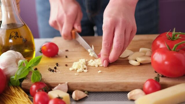 making pasta carbonara - cut garlic with knife on a wooden cutting board