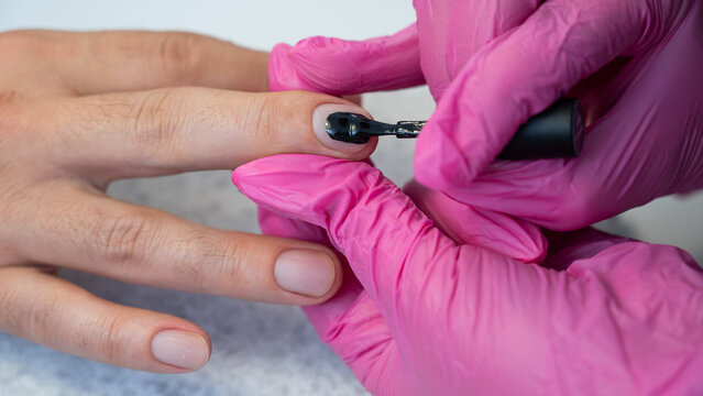 A man on a manicure procedure paints his nails black in a beauty salon