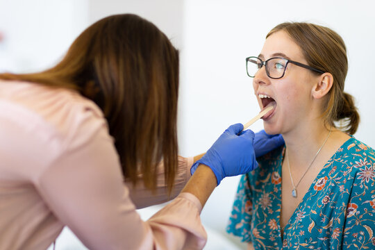 Young female with mouth open being checked by doctor
