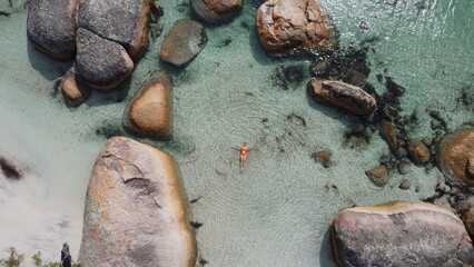 Aerial picture of a girl swimming in a fairy pool in Albany, Western Australia. Shallow and transparent water. Drone topdown.Girl with orange swimsuit. Swimming in paradise in blue water between rocks © Elsa