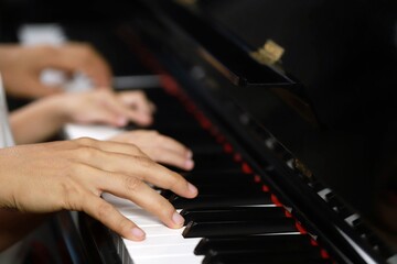 Fototapeta na wymiar Select the focus on the piano trainer fingers and piano keys to play the piano. There are musical instruments for concerts or music lessons. Close-up of child musicians playing piano on stage