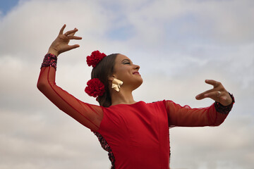 Portrait of young teenage woman in red dance suit with red carnations in her hair doing flamenco...