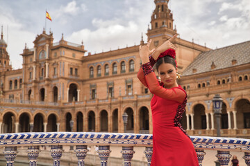 Obraz premium Young teenage woman in red dance suit with red carnations in her hair doing flamenco dance poses. Flamenco concept, dance, art, typical Spanish dance.