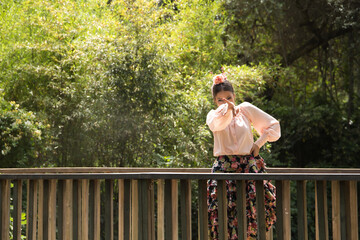 Young teenage woman in pink shirt, black skirt with flowers and pink carnations in her hair, dancing flamenco on wooden bridge. Flamenco concept, dance, art, typical Spanish dance.