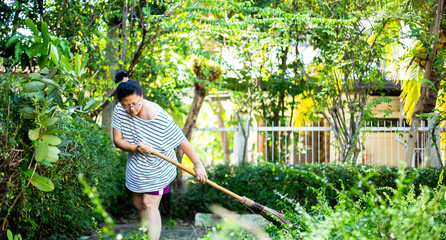 Asian woman sweeping leaves in the garden.