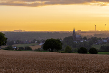 Colourful sunrise in the only Dutch mountain village located in the south of Limburg, with a view on a spectacular sky, the tower of the catholic church , the vineyards and agricultural grain fields 