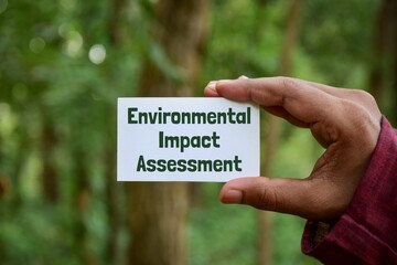 Man holding card with the text Environmental Impact Assessment (EIA) in the park. Selective focus.
