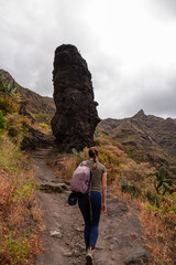 Woman walking next to massive rock formation wall in the Canyon Barranco de Afur, Anaga park,...