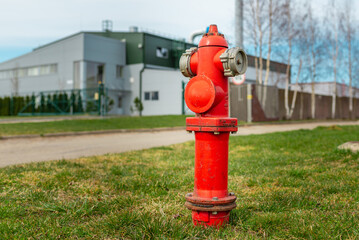 Fototapeta na wymiar Single red fire hydrant on green lawn.In a background factory.Autumn,spring,summer day.Closeup.