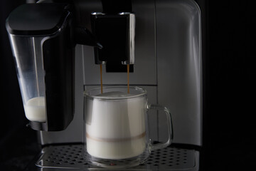 Freshly brewed cappuccino is poured from the coffee machine into glass cups.