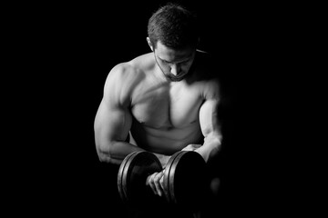 Handsome power athletic man with dumbbell confidently looking forward. Strong bodybuilder with six pack, perfect abs, shoulders, biceps, triceps and chest. Strength and motivation