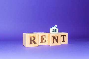 Wooden cubes with word RENT with miniature toy house on a purple,veri peri background.