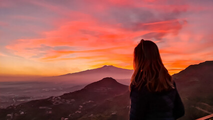 Tourist woman watching beautiful sunset behind volcano Mount Etna near Castelmola, Taormina,...
