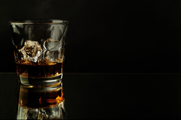 crystal glass with ice and whiskey with reflection on dark background and copy space