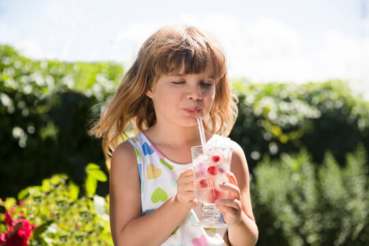 little child girl drinks a cool drink with flower ice cubes and berry ice cubes  cubes on a hot summer day