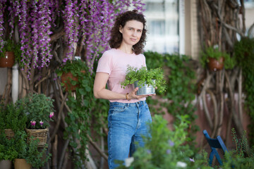 middle aged woman holding pot with mixed green fresh aromatic herbs in garden near the house.