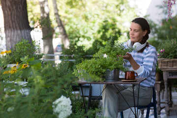 middle aged woman holding pot with mixed green fresh aromatic herbs in garden near the house.