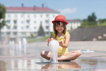 Child girl playing and having fun in fountains  in the city r on sunny summer day. 