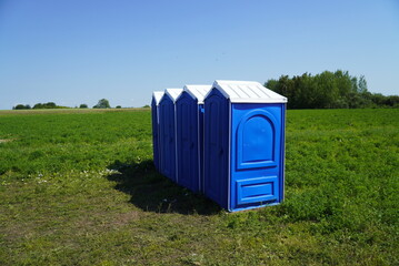 Portable plastic toilets in the field on the grass on a background of blue sky.