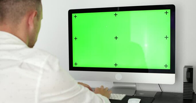 Green screen. Employee working at computer sitting at desk. View from back.