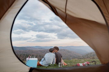 View from inside tent on beautiful landscape of mountains and couple kissing. Love and travel. 