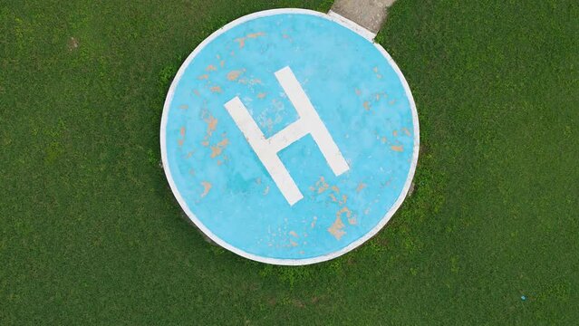 Blue landing pad on green grass top view. Helicopter parking. Markings, signs and pointers.