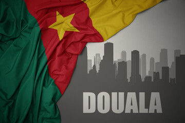 abstract silhouette of the city with text Douala near waving colorful national flag of cameroon on a gray background.