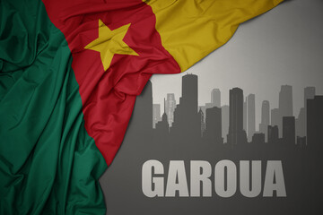 abstract silhouette of the city with text Garoua near waving colorful national flag of cameroon on a gray background.