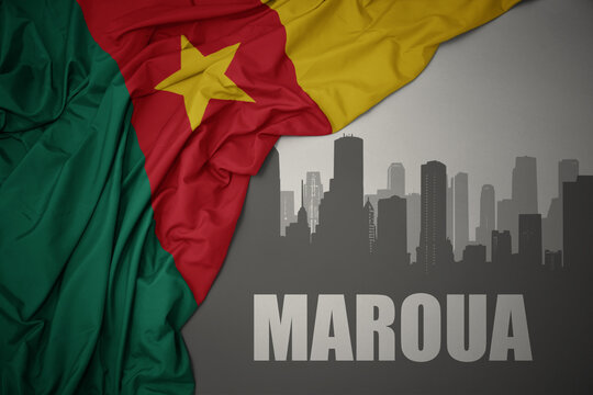 abstract silhouette of the city with text Maroua near waving colorful national flag of cameroon on a gray background.