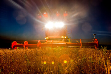 Combine harvester working in wheat field at dark night. Agriculture background. Harvest season
