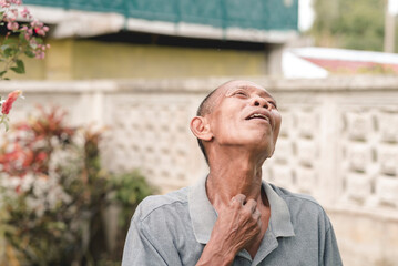 An older man touches his parched throat, feeling thirsty after a long day. Outdoor scene.